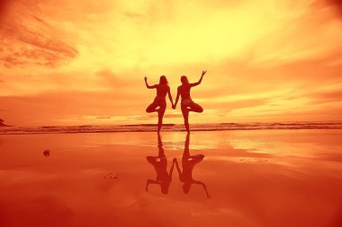 meditasyon ve yoga sahilde. Deniz kıyısında yoga yaparken iki genç kadın