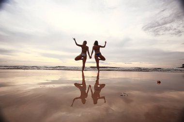 meditasyon ve yoga sahilde. Deniz kıyısında yoga yaparken iki genç kadın