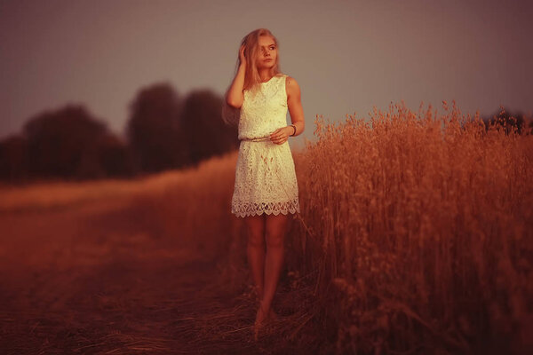 Beautiful young woman in rural field at sunset, summer vacation