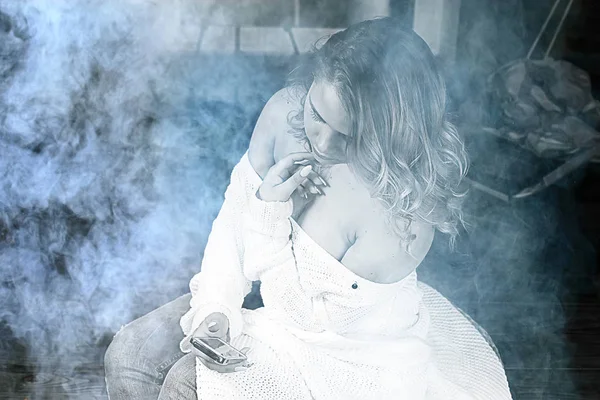 白色针织毛衣的年轻金发女子摆在黑暗的房间与烟雾 — 图库照片