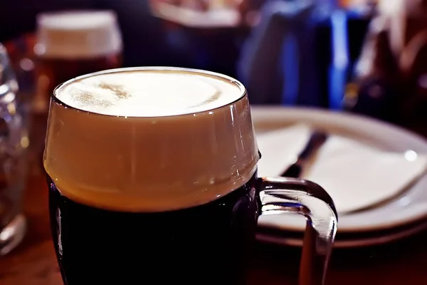 チェコ共和国でのレストランでお召し上がりいただけますテーブル上の泡とビールのパイントのパブの内部に黒ビールのマグカップ — ストック写真