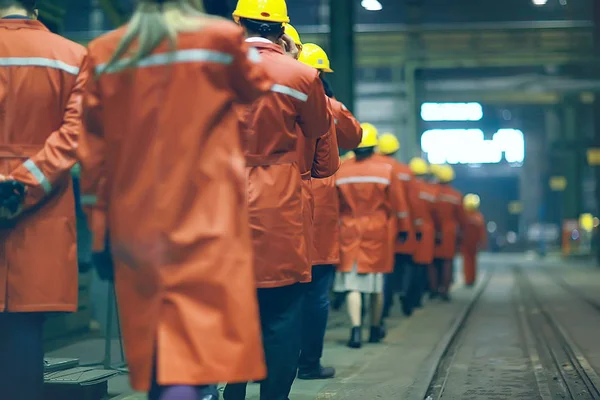 group of workers in helmets at the factory, view from the back