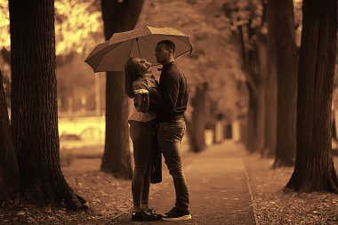 bir şemsiye altında iki kişi/bir erkek ve bir kadın bir şemsiye ile bir parkta yürüyüş, yağmur sonbaharda yürüyüş, bir sonbahar şemsiyesi