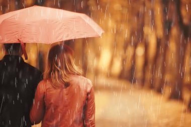 Sonbahar parkında yağmur/genç 25 yaşında çift adam ve kadın ıslak yağmurlu havalarda bir şemsiye altında yürümek, Ekim severler yürümek
