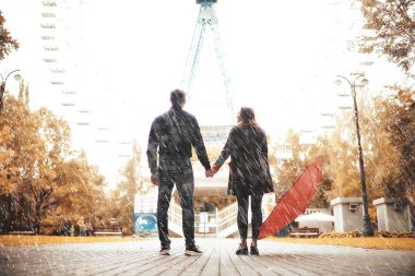 Sonbahar parkında yağmur/genç 25 yaşında çift adam ve kadın ıslak yağmurlu havalarda bir şemsiye altında yürümek, Ekim severler yürümek