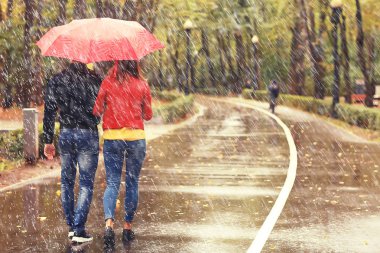 Sonbahar parkında yağmur/genç 25 yaşında çift adam ve kadın ıslak yağmurlu havalarda bir şemsiye altında yürümek, Ekim severler yürümek