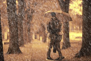 Sonbahar parkında yağmur/genç 25 yaşında çift adam ve kadın ıslak yağmurlu havalarda bir şemsiye altında yürümek, Ekim severler yürümek