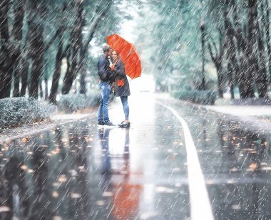 Sonbahar parkında yağmur/genç 25 yaşında çift adam ve kadın ıslak yağmurlu havalarda bir şemsiye altında yürümek, Ekim severler yürümek