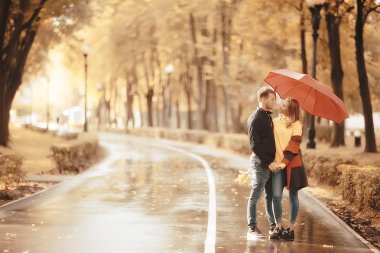 Sonbahar parkında güneş ışınları, aşık bir çift/genç adam ve kadın yürüyüş, güneşli parkın sonbahar görünümü, güneşin ışınları, sıcak sonbahar arka plan