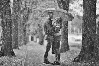 Sonbahar parkında yağmur/genç 25 yaşında çift adam ve kadın ıslak yağmurlu havalarda bir şemsiye altında yürümek, Ekim severler yürümek