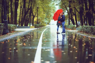 Sonbahar parkında yağmur/genç 25 yaşında çift adam ve kadın ıslak yağmurlu havalarda bir şemsiye altında yürümek, Ekim severler yürümek