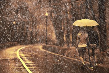 Sonbahar parkında yağmur/genç 25 yaşında çift adam ve kadın ıslak yağmurlu havalarda bir şemsiye altında yürümek, Ekim severler yürümek