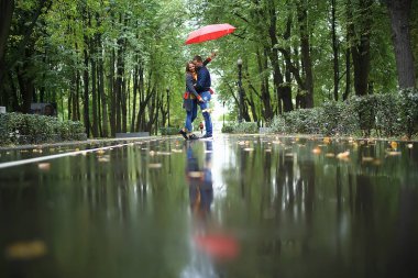 bir şemsiye altında iki kişi/bir erkek ve bir kadın bir şemsiye ile bir parkta yürüyüş, yağmur sonbaharda yürüyüş, bir sonbahar şemsiyesi