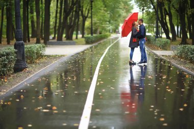 Sonbahar parkında yağmur/genç 25 yaşında çift adam ve kadın ıslak yağmurlu havalarda bir şemsiye altında yürümek, Ekim severler yürümek