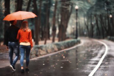 Sonbahar parkında yağmur/genç 25 yaşında çift adam ve kadın ıslak yağmurlu havalarda bir şemsiye altında yürümek, Ekim severler yürümek