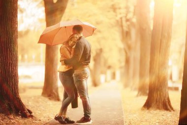 Sonbahar parkında güneş ışınları, aşık bir çift/genç adam ve kadın yürüyüş, güneşli parkın sonbahar görünümü, güneşin ışınları, sıcak sonbahar arka plan