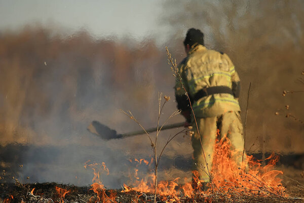 firefighter puts out grass / forest fire, dry grass burns, wind blows