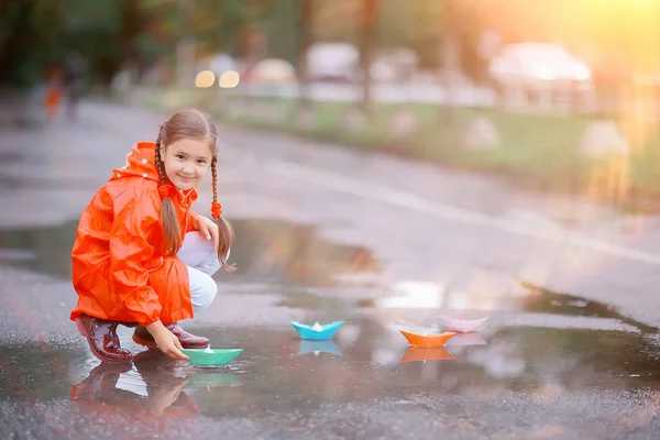 女の子は水たまりで紙ボートで遊ぶ 公園の秋の散歩 子供は雨の中で遊ぶ — ストック写真