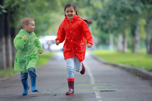 子供たちはレインコート サマーパーク 歩く兄弟姉妹 子供の男の子と女の子で実行します — ストック写真