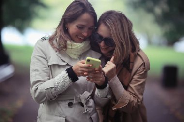 iki kız telefon sonbahar yürüyüş / sonbahar şehir parkı ceket, sonbahar moda, stil, bakmak, giysi bakmak