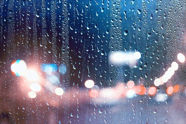 drops on glass auto road rain autumn night / abstract autumn background in the city, auto traffic, romantic trip by car