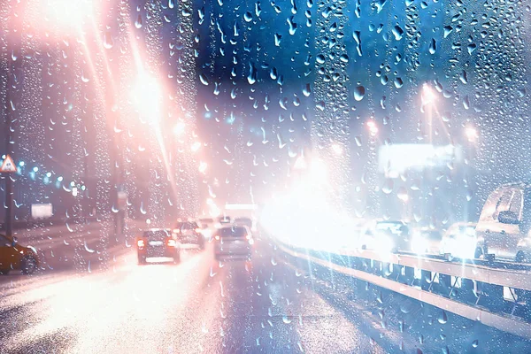 drops on glass auto road rain autumn night / abstract autumn background in the city, auto traffic, romantic trip by car