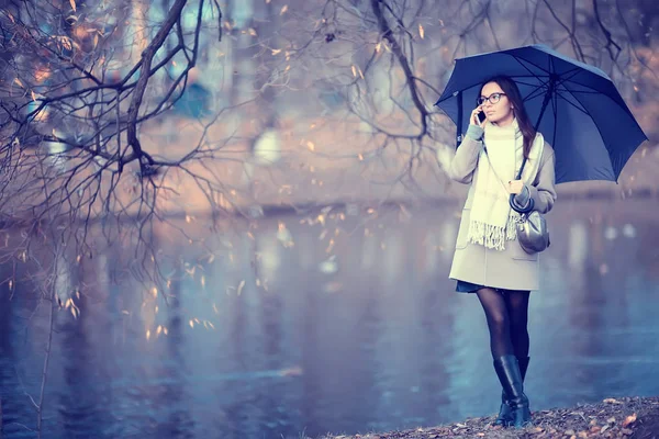 woman talking on the phone in the fall rain / autumn weather message about the rain, a model with an umbrella