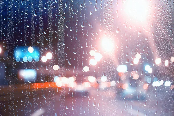 drops on glass auto road rain autumn night / abstract autumn background in the city, auto traffic, romantic trip by car