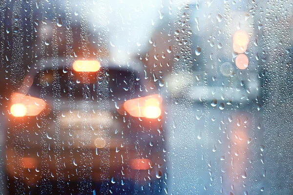 drops on glass auto road rain autumn night / abstract autumn background in the city, auto traffic, romantic trip by car