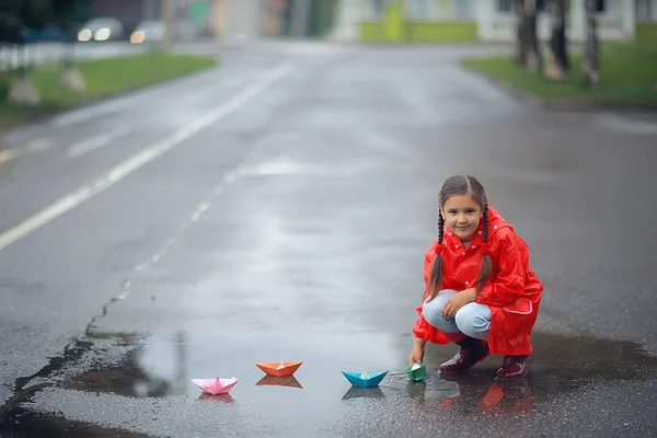 女の子は水たまりで紙ボートで遊ぶ 公園の秋の散歩 子供は雨の中で遊ぶ — ストック写真