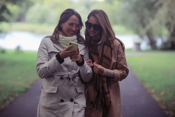 Dos Chicas Miran Teléfono Otoño Paseo Otoño Ciudad Parque Abrigo —  Fotos de Stock