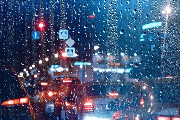 drops on glass auto road rain autumn night / abstract autumn background in the city, auto traffic, romantic trip by car