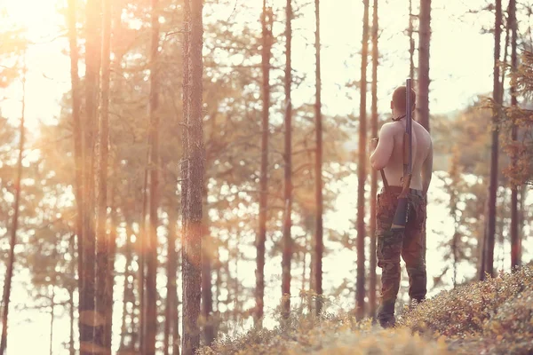 hunting man / hunter with a gun hunting in the autumn forest, yellow trees landscape in the taiga