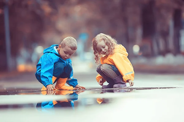 兄弟と姉妹は水たまり レインコートの服でボートを再生し 秋の天気の子供たちは紙のボートを再生します — ストック写真