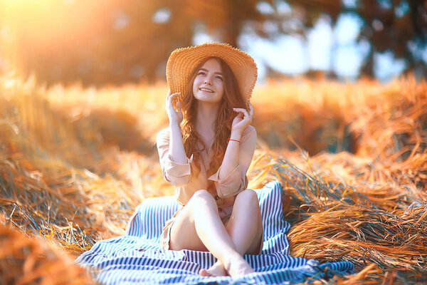 Girl sitting in a field with a straw hat / summer vacation, rest young adult happy woman