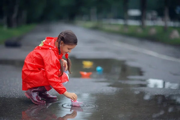 女の子は水たまりで紙ボートで遊ぶ 公園の秋の散歩 子供は雨の中で遊ぶ — ストック写真