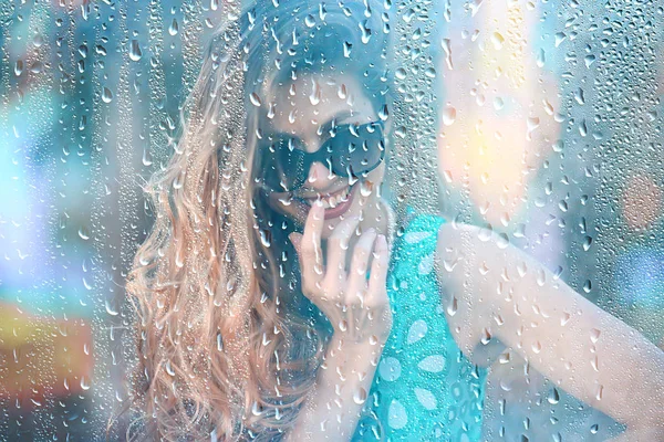 young adult girl outside the window view in the rain / raindrops on the glass warm autumn rain seasonal view