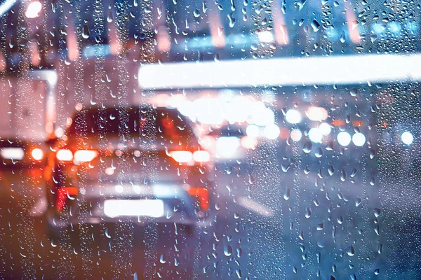drops on glass auto road rain autumn night / abstract autumn background in the city, auto traffic, romantic trip by car