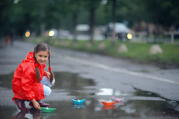 女の子は水たまりで紙ボートで遊ぶ 公園の秋の散歩 子供は雨の中で遊ぶ — ストック写真