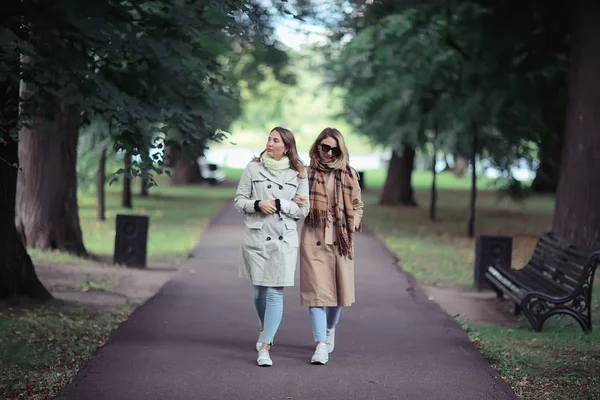 秋のファッションパークの女の子2ルック コートで2人の魅力的なファッショナブルなガールフレンドが都市公園を歩く — ストック写真