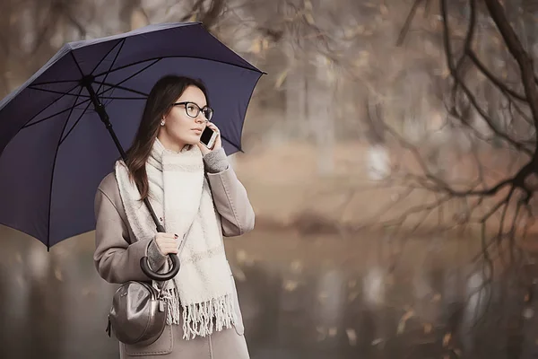 woman talking on the phone in the fall rain / autumn weather message about the rain, a model with an umbrella