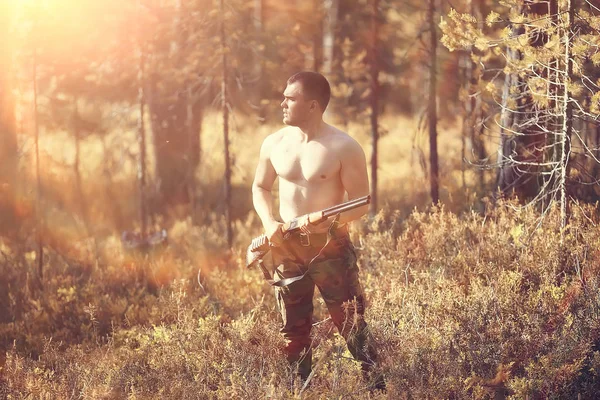 hunting man / hunter with a gun hunting in the autumn forest, yellow trees landscape in the taiga