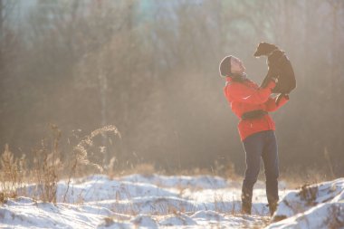 Kışın güneşli çayırda arkadaşı köpek tutan mutlu adam Portresi