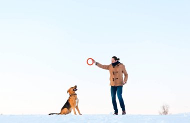 Adam kış manzara büyük karışık cins köpek ile oynuyor.