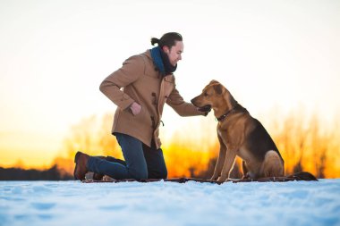 Adam kış manzara büyük karışık cins köpek ile oynuyor.