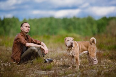 Bir adam ve bir shar pei cins köpek bir çayırda yerde oturan Portresi