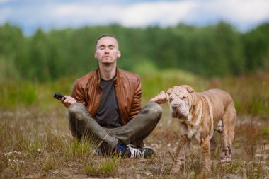 Bir adam ve bir shar pei cins köpek bir çayırda yerde oturan Portresi