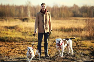 Genç mutlu Avrupa gülümseyen ve iki köpek ile bir alanda ayakta gülüyor