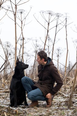 Bir kış çayırında yürüyen melez bir köpekle yürüyen bir adam.