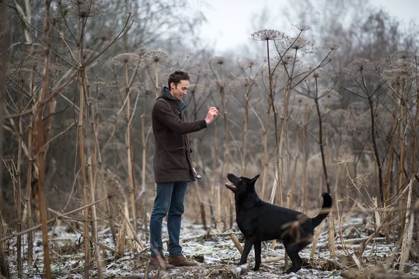 Ein Mann mit einem Mischlingshund beim Gassigehen auf einer Winterwiese — Stockfoto